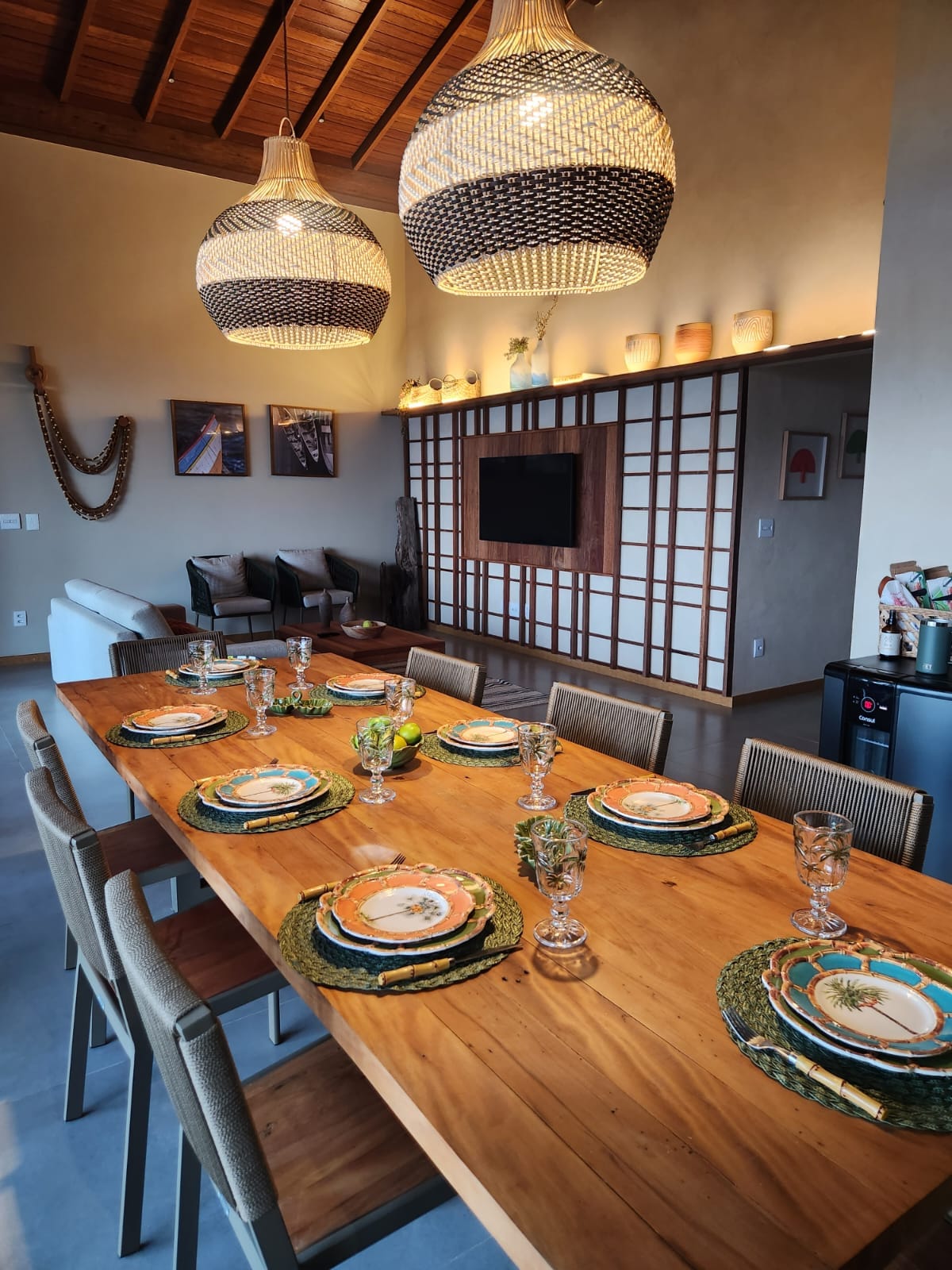 Sala de jantar com mesa de madeira para dez, luminárias artesanais e painéis shoji