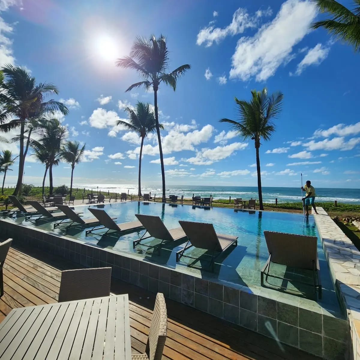 Piscina à beira-mar do condomínio com deck de madeira e coqueiros