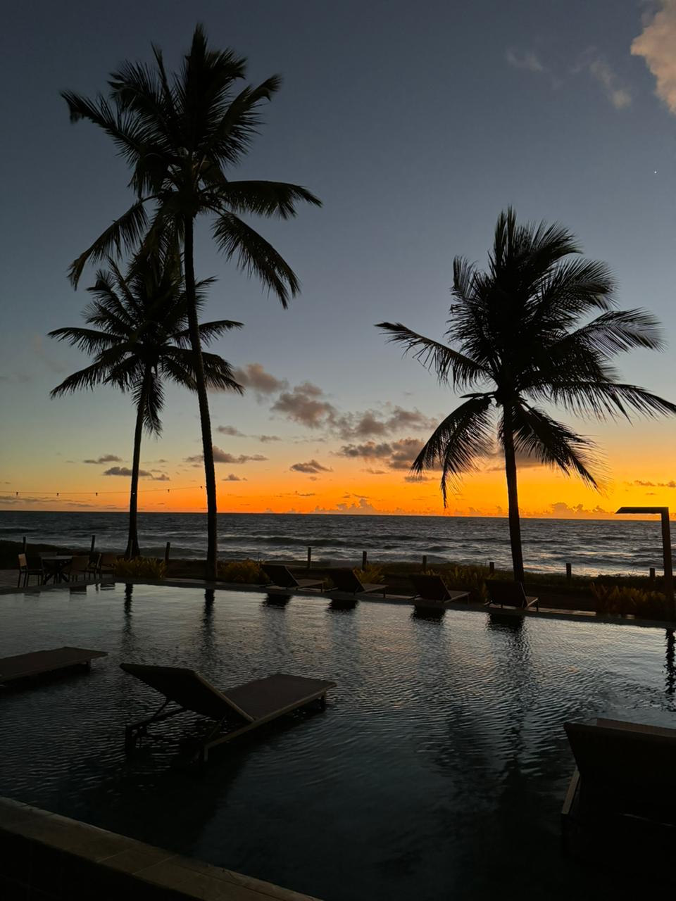 Piscina principal ao pôr do sol entre coqueiros