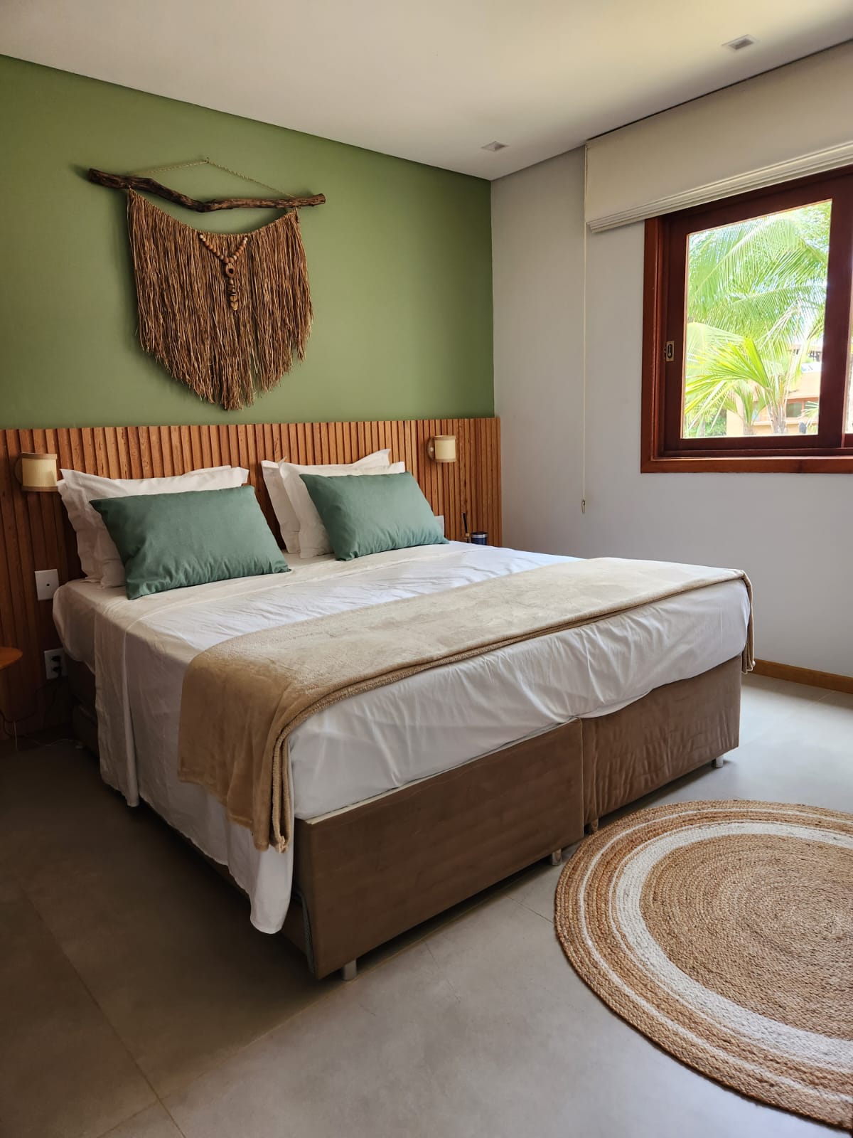 Suíte com parede verde, cabeceira ripada em madeira e janela para o jardim tropical