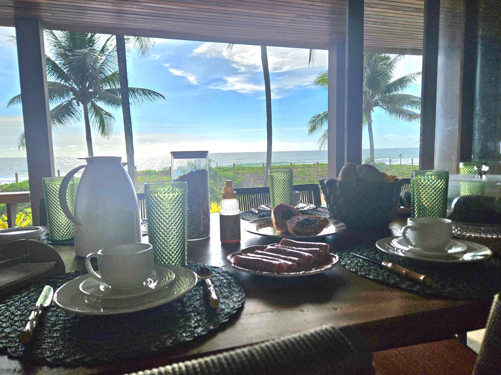 Mesa de café da manhã com vista panorâmica para o mar entre coqueiros