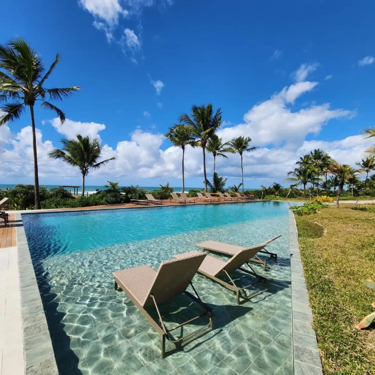 Piscina infinita do condomínio com espreguiçadeiras dentro d'água e vista para o mar